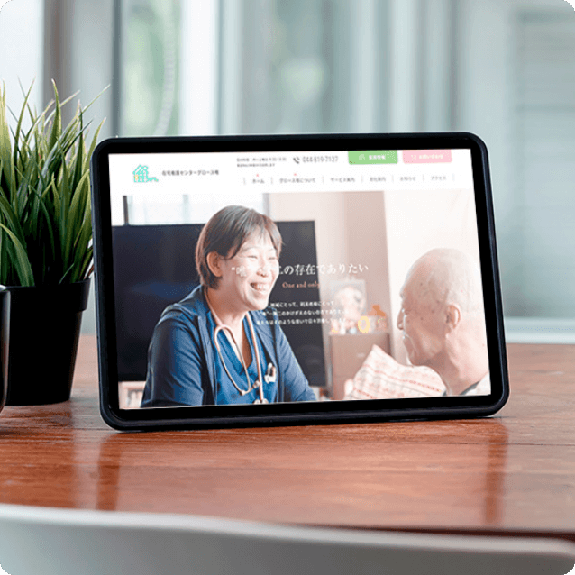 タブレット画面に、医療スタッフが患者と笑顔で会話しているウェブサイトが表示されている。背面には観葉植物が置かれている。