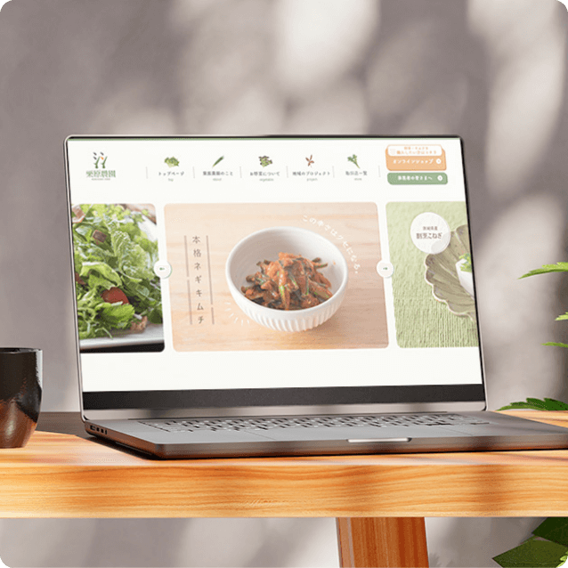 ノートパソコンに、様々な食材や料理の画像が並ぶウェブサイトが表示されている。デスクには植物とコーヒーカップが置かれている。